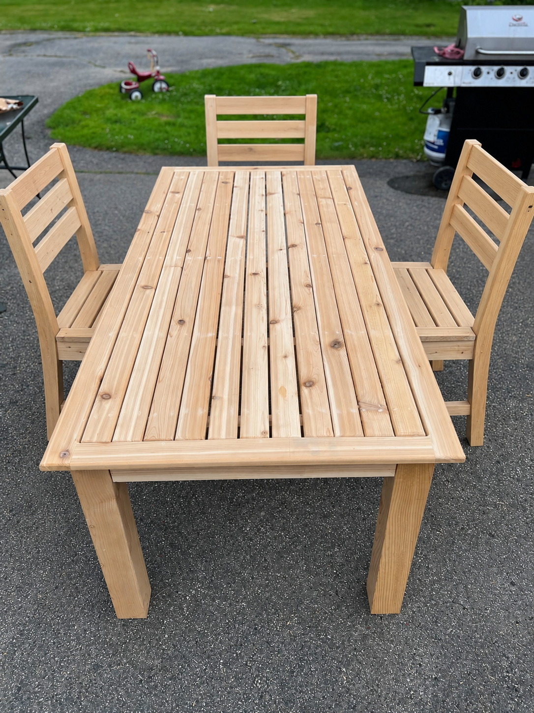 Solid wood slatted-top dining table with matching ladder-back chairs, shown outdoors on a driveway