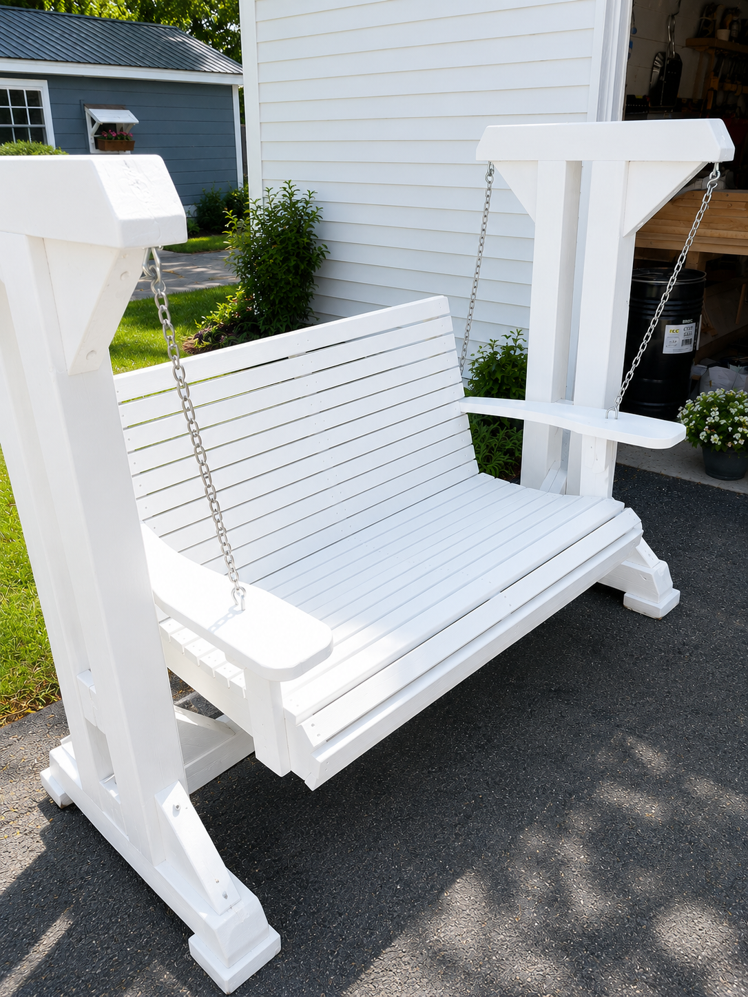 Close-up view of a white-painted wooden porch swing with slatted seat and back, hanging by chains from a matching black-stained wood A-frame stand.