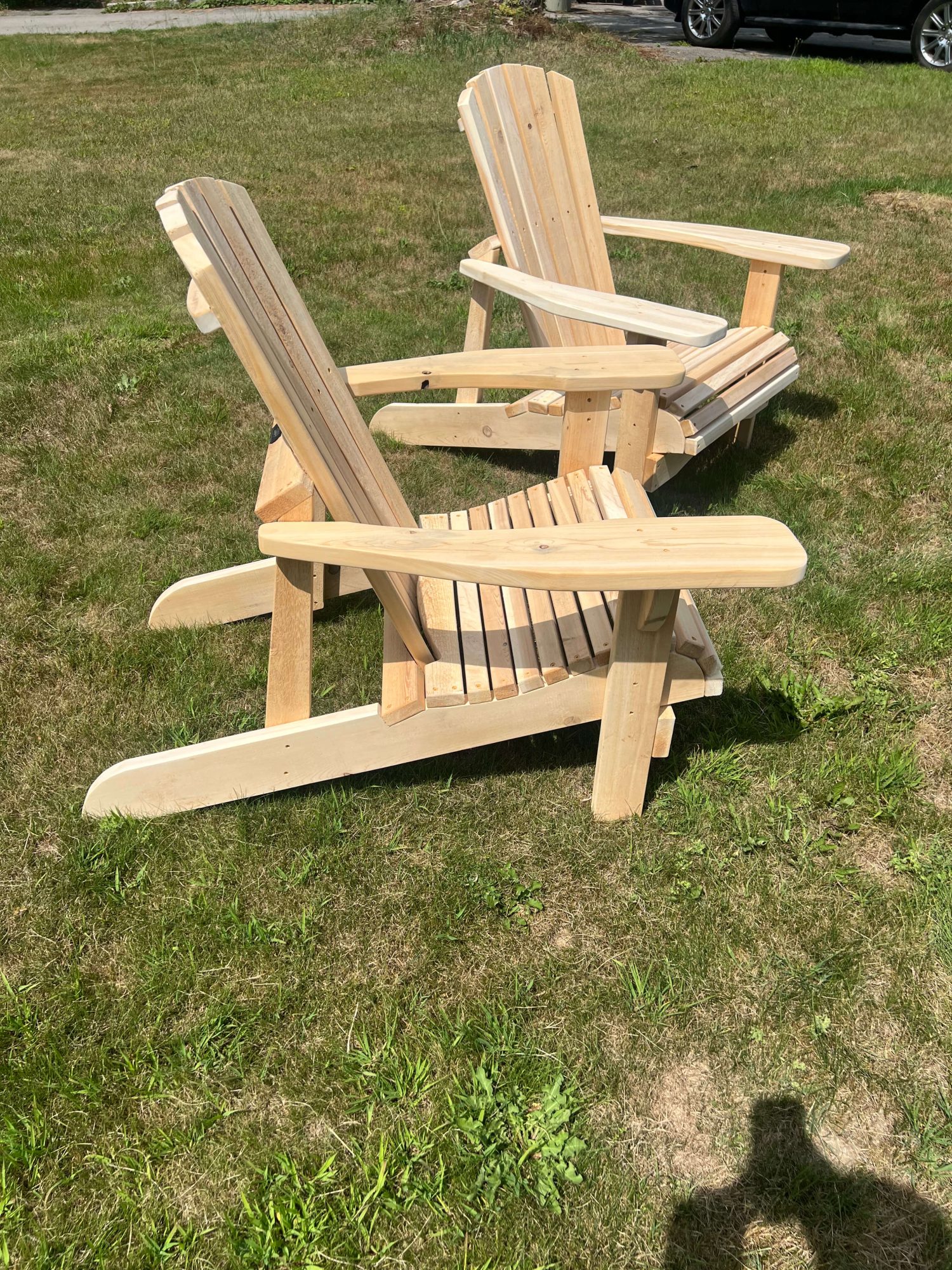Two natural-finish wood Adirondack chairs positioned side by side on grass, showcasing the fanned slat backs and wide flat armrests.